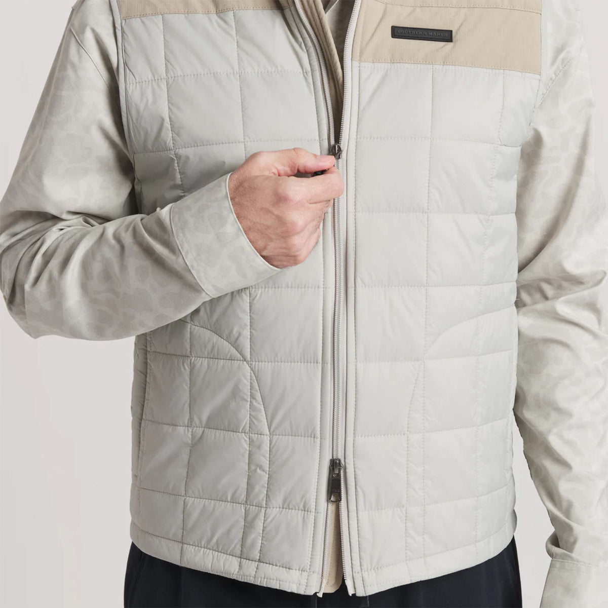 Person wearing a beige quilted jacket with a neutral background