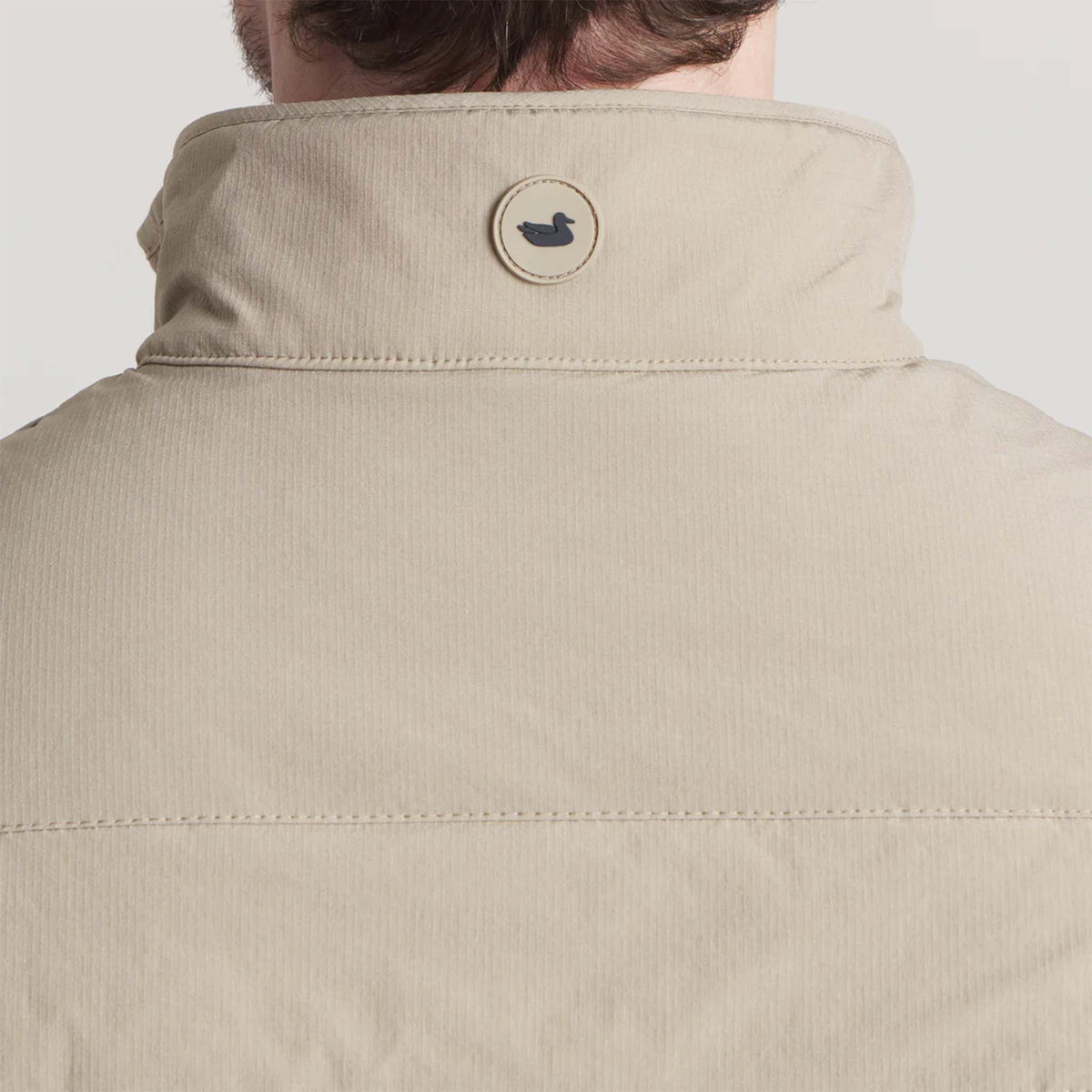 Beige jacket with a brand logo on the collar against a light gray background