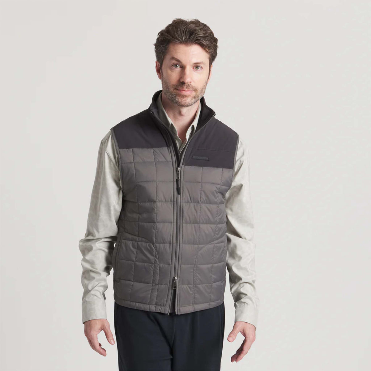 Man wearing a gray quilted vest over a light shirt on a white background