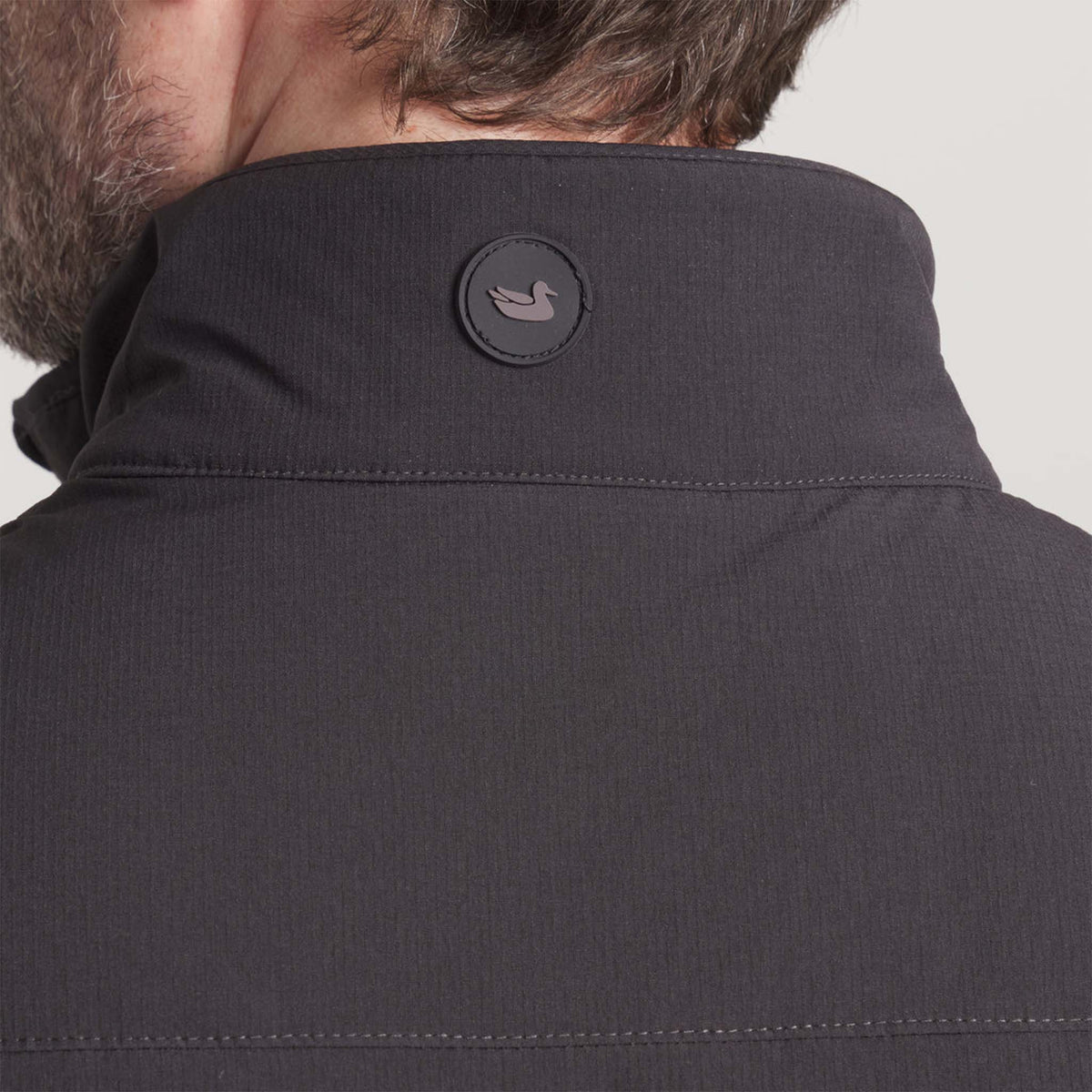 Close-up of a dark gray jacket with a brand logo on the collar against a light gray background