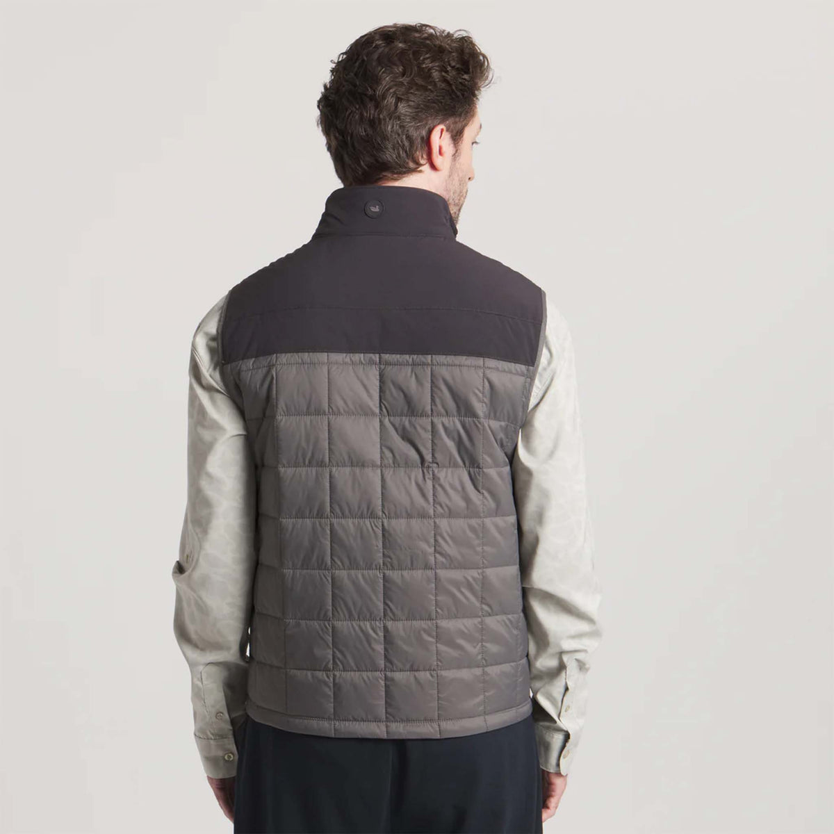 Person wearing a black and gray quilted vest on a light gray background