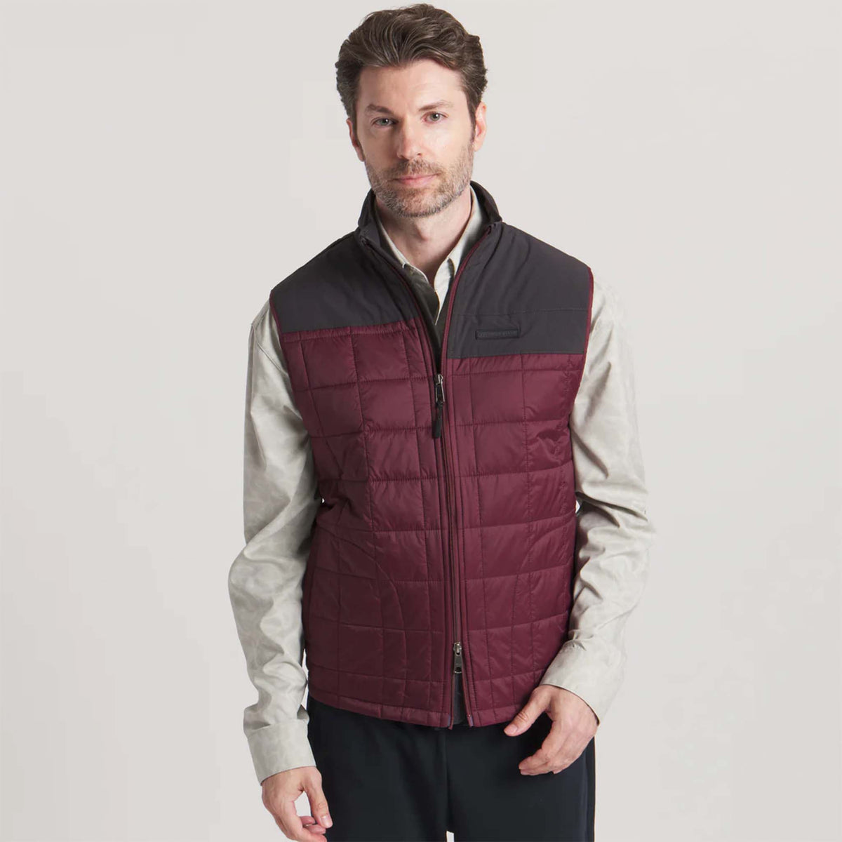 Man wearing a two-tone quilted vest with maroon and black sections on a light gray background