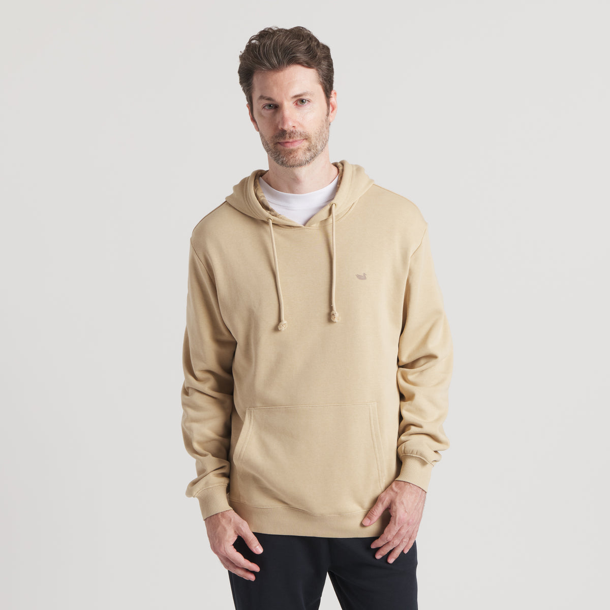 Front view of model wearing tan hoodie with kangaroo pocket and drawstrings.