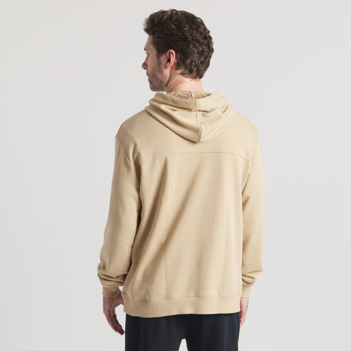 Man wearing a beige hoodie from behind on a plain background