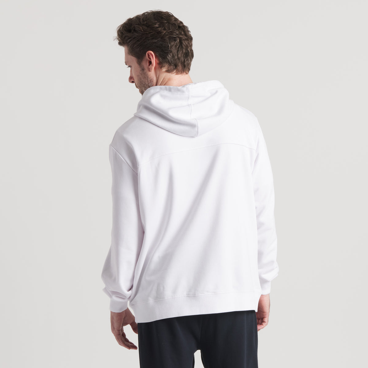 Back view of model wearing white hoodie with hood down and relaxed fit.