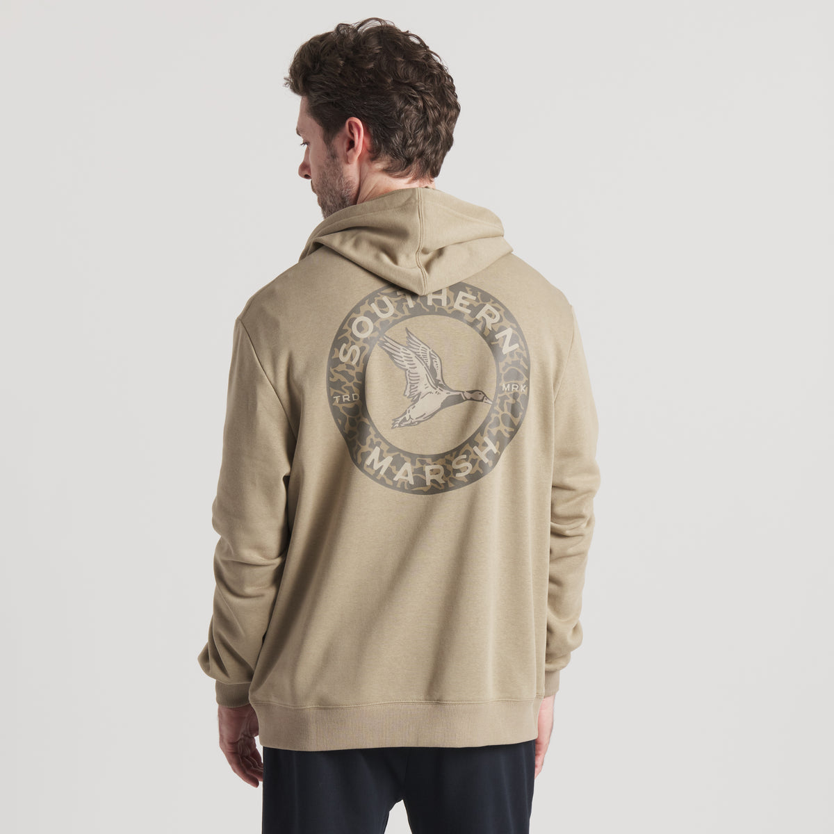 Man wearing a beige hoodie with a logo on the back against a white background