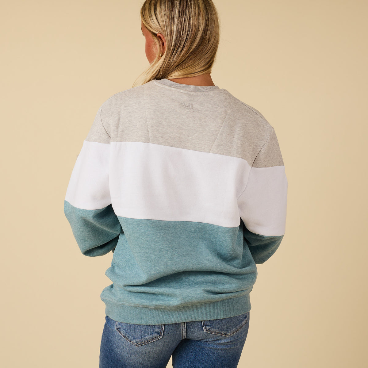 Person wearing a color-blocked sweater with beige, white, and blue sections on a beige background