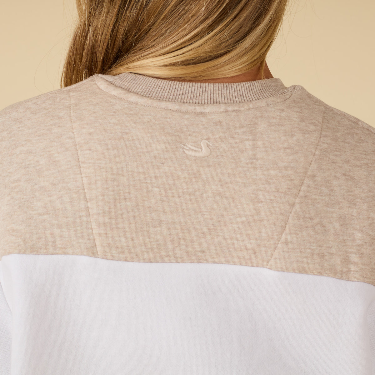 Close-up of a person wearing a beige sweater with a logo, on a beige background
