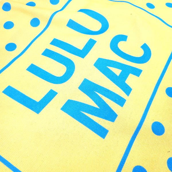 Bright yellow canvas tote bag with turquoise blue polka dot pattern and 'LULU MAC' branding on a white background