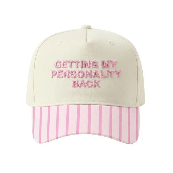 Cream baseball cap with pink embroidered “Getting My Personality Back” text and pink striped brim.
