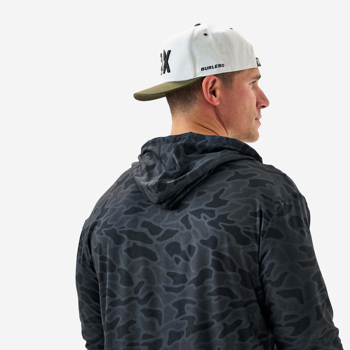 Man wearing a camouflage hoodie and a cap with a brand logo on a white background