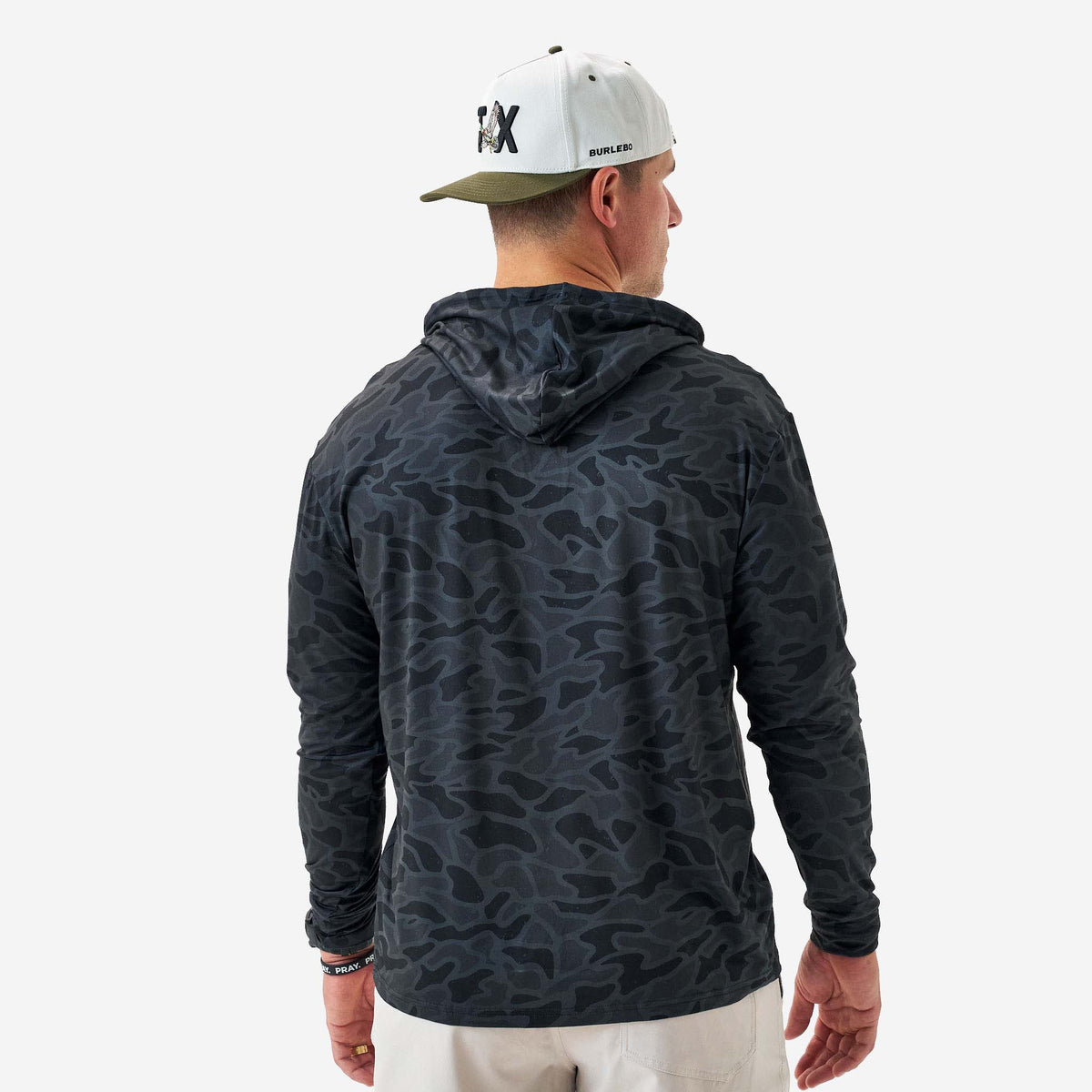 Person wearing a dark camouflage hoodie and a cap on a white background