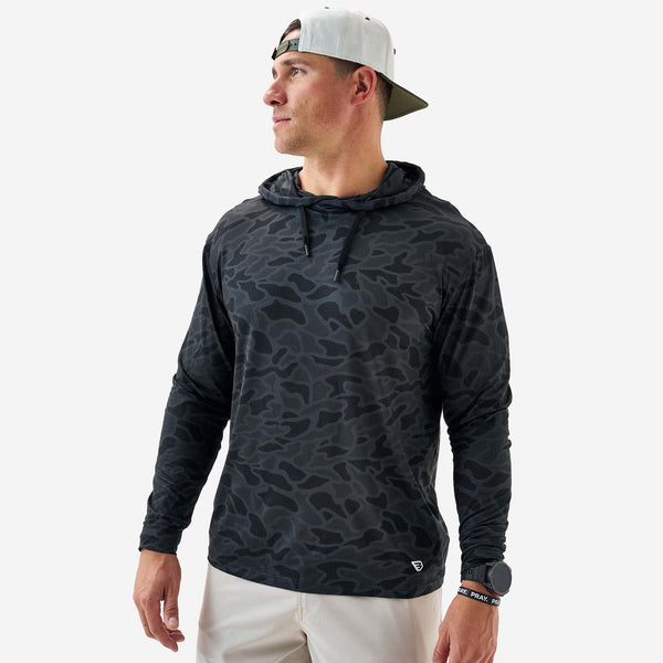 Man wearing a black camouflage hoodie and white pants on a white background