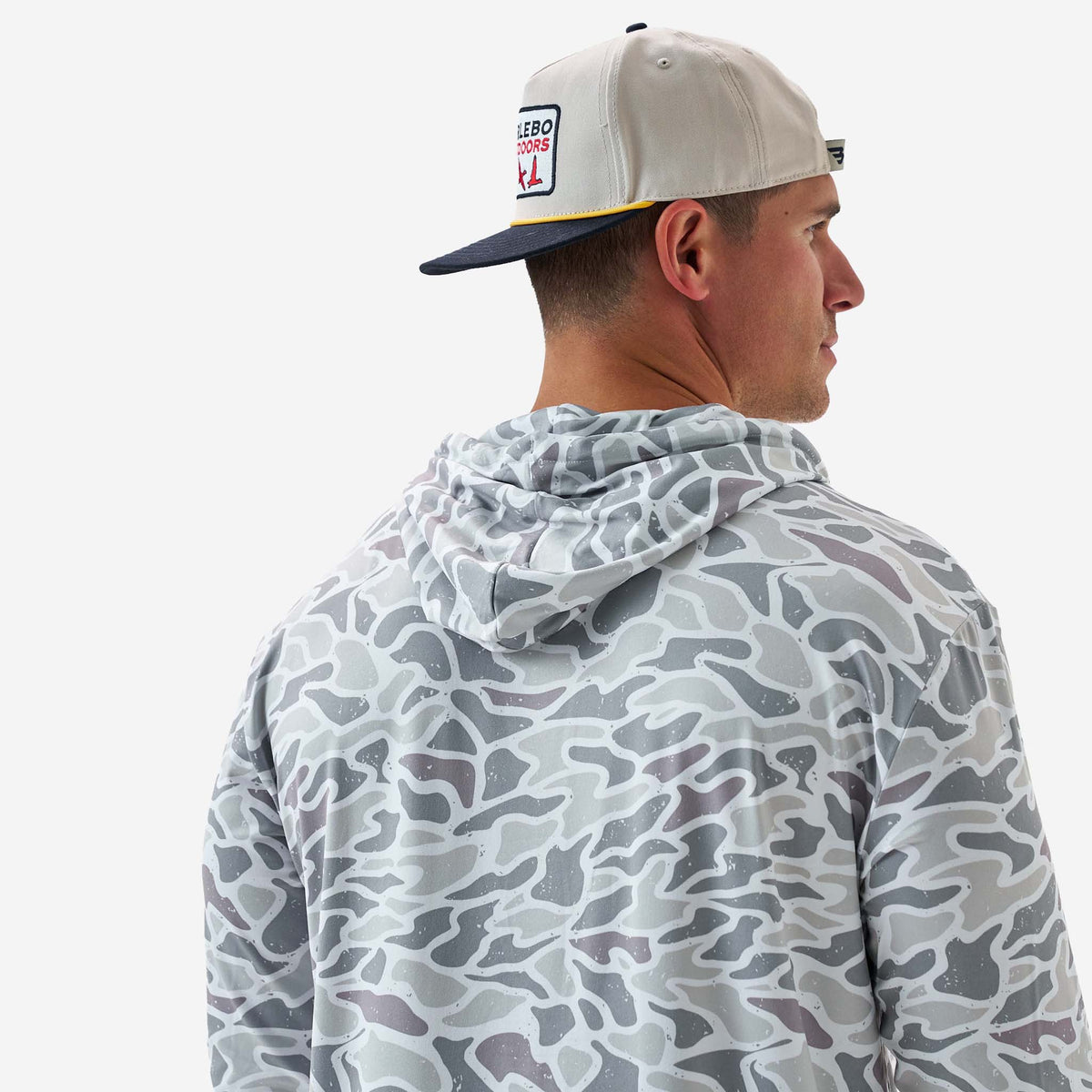 Person wearing a camouflage hoodie and cap with a visible brand logo on a white background