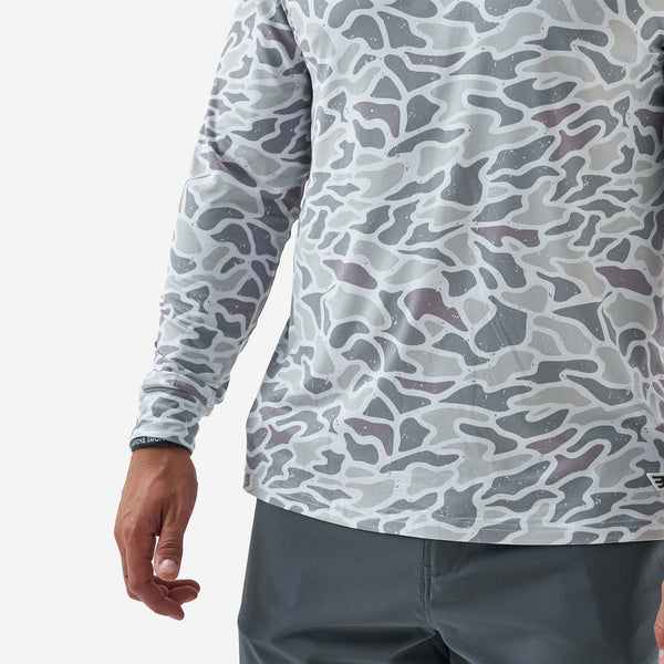 Person wearing a long-sleeve shirt with a camouflage pattern on a plain background