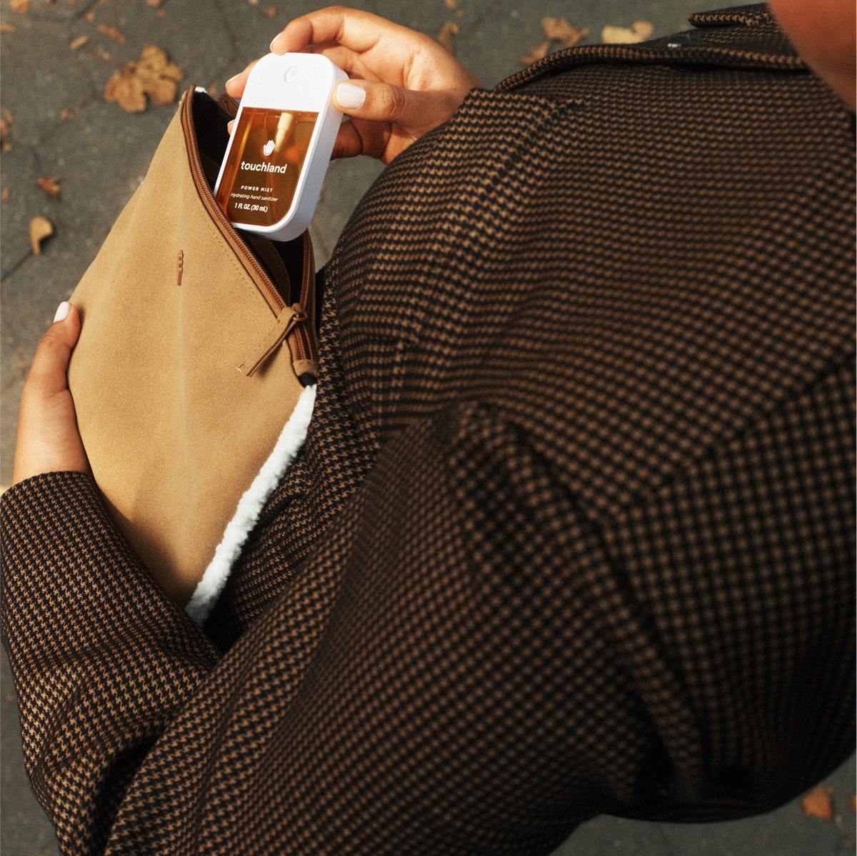Person holding a brown leather jacket with fur lining and a bottle of touchless hand sanitizer.