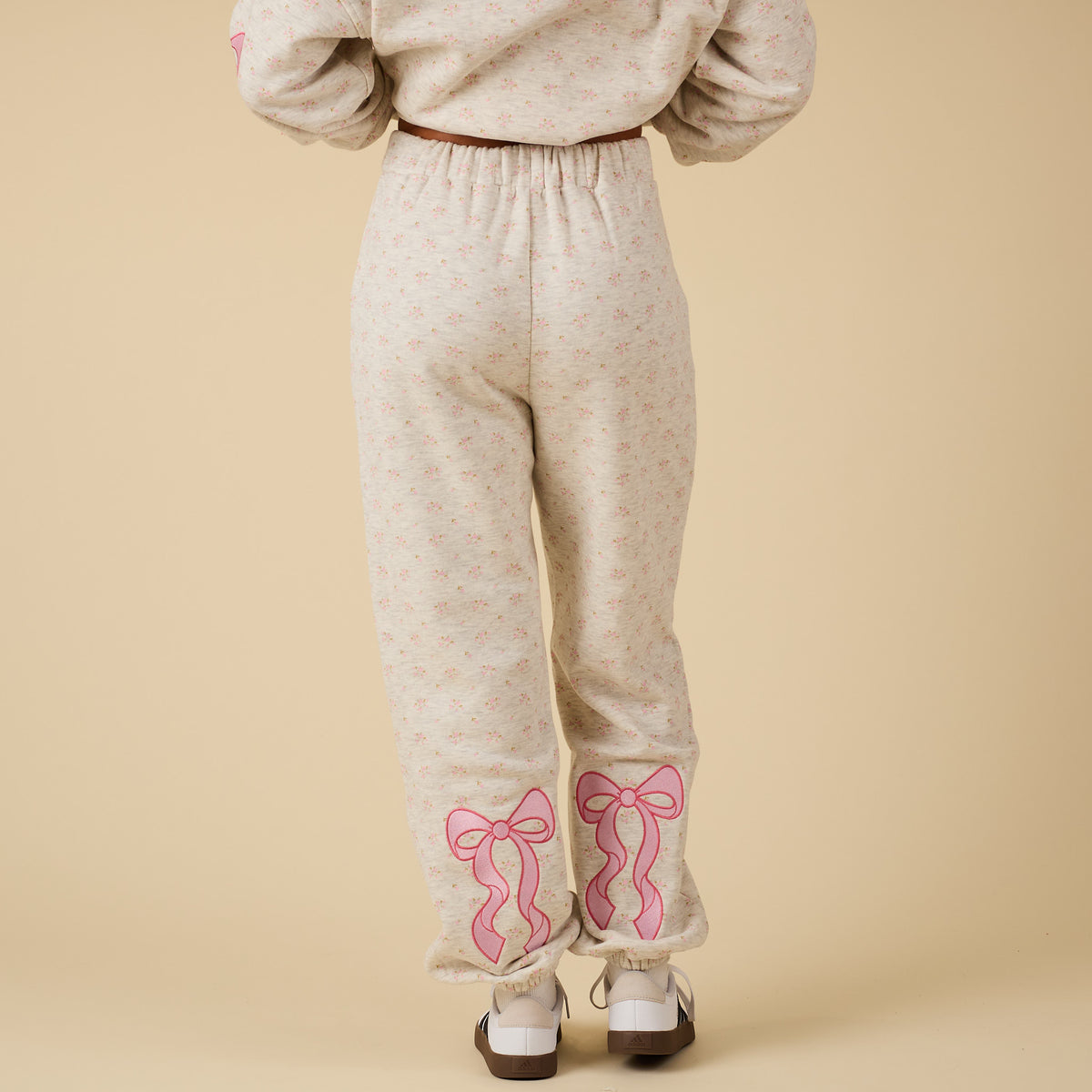 Back view of model wearing Alice Pink Bow Sweatpants with pink bow embroidery on lower legs.