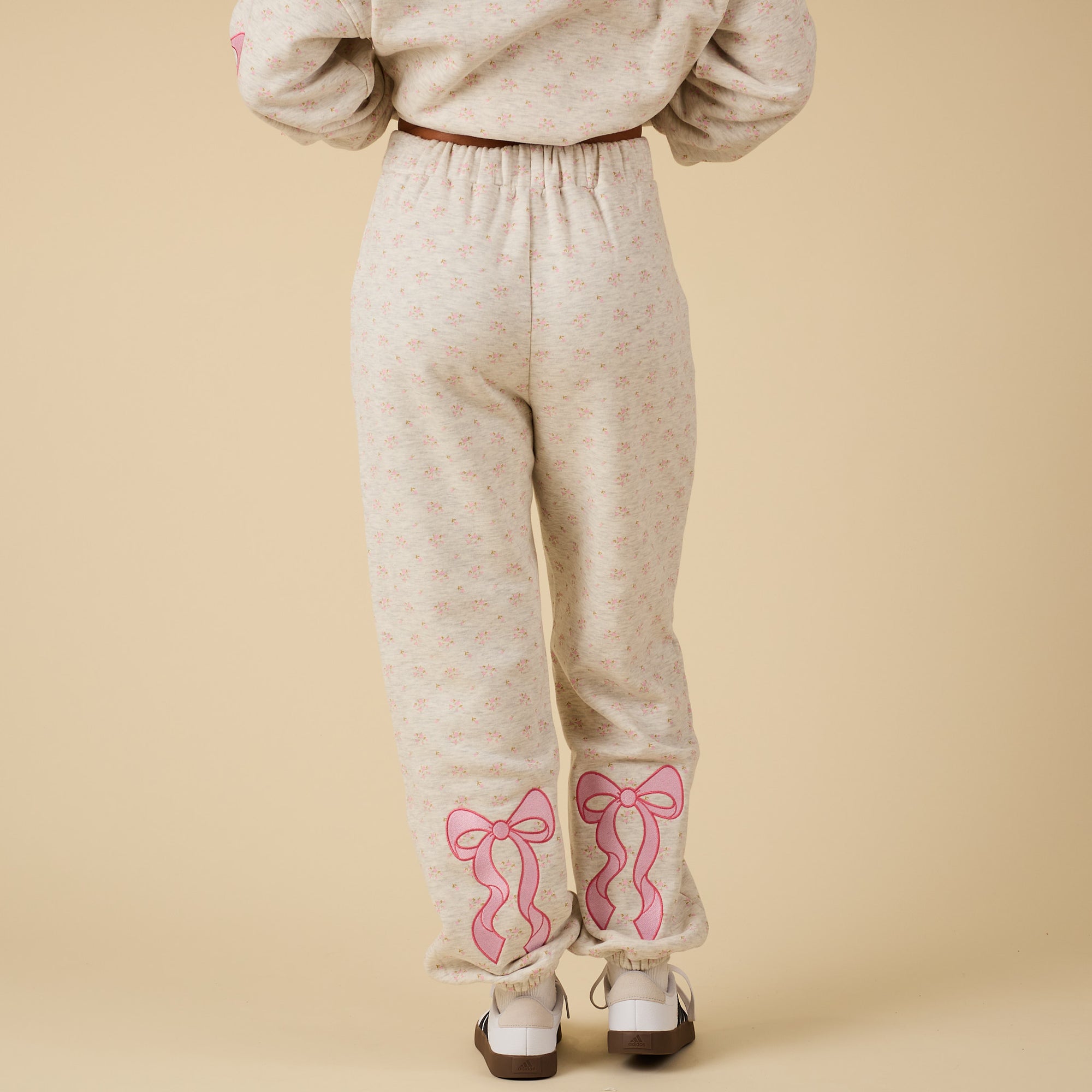 Back view of model wearing Alice Pink Bow Sweatpants with pink bow embroidery on lower legs.