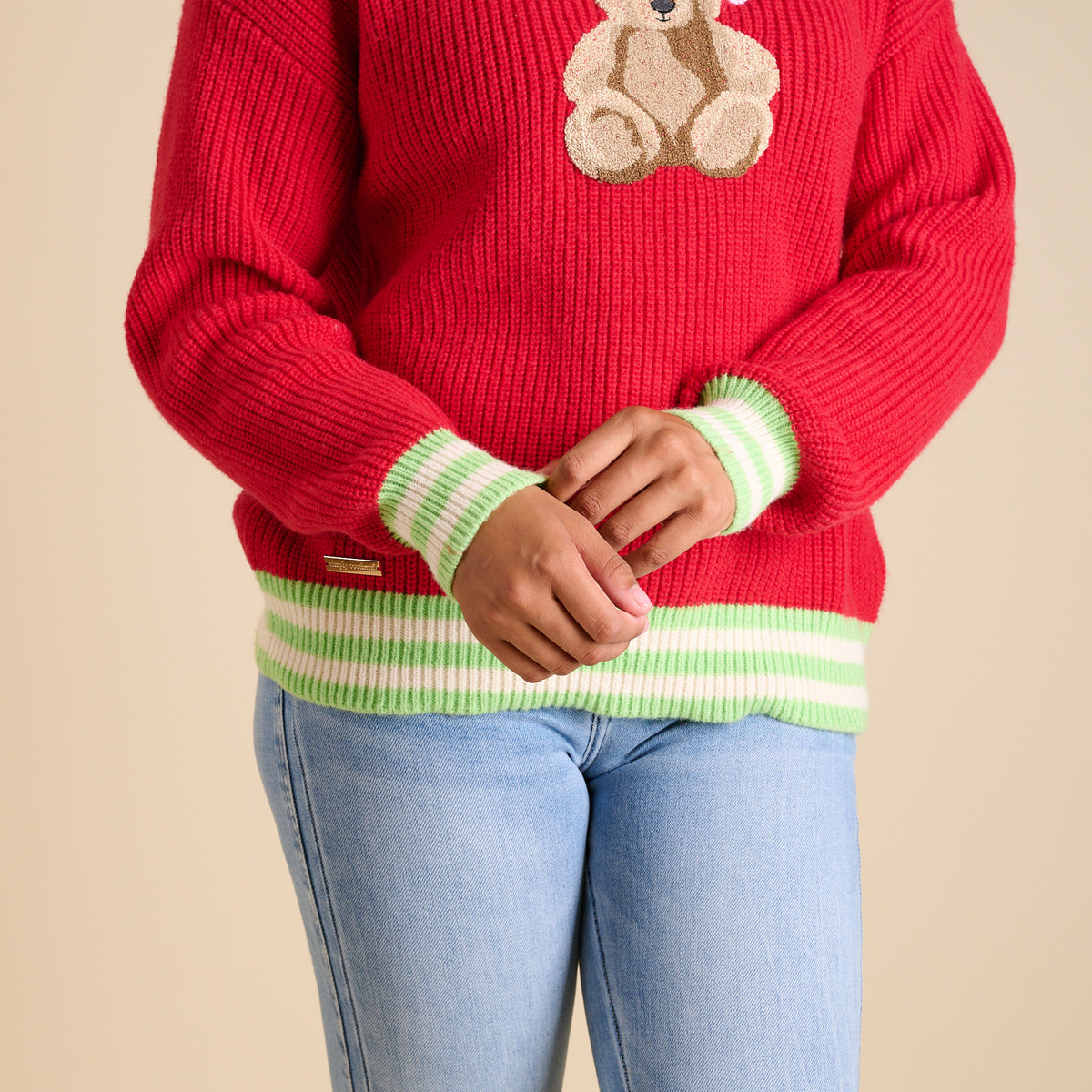 Red knit sweater with green-and-white striped trim and teddy bear graphic.