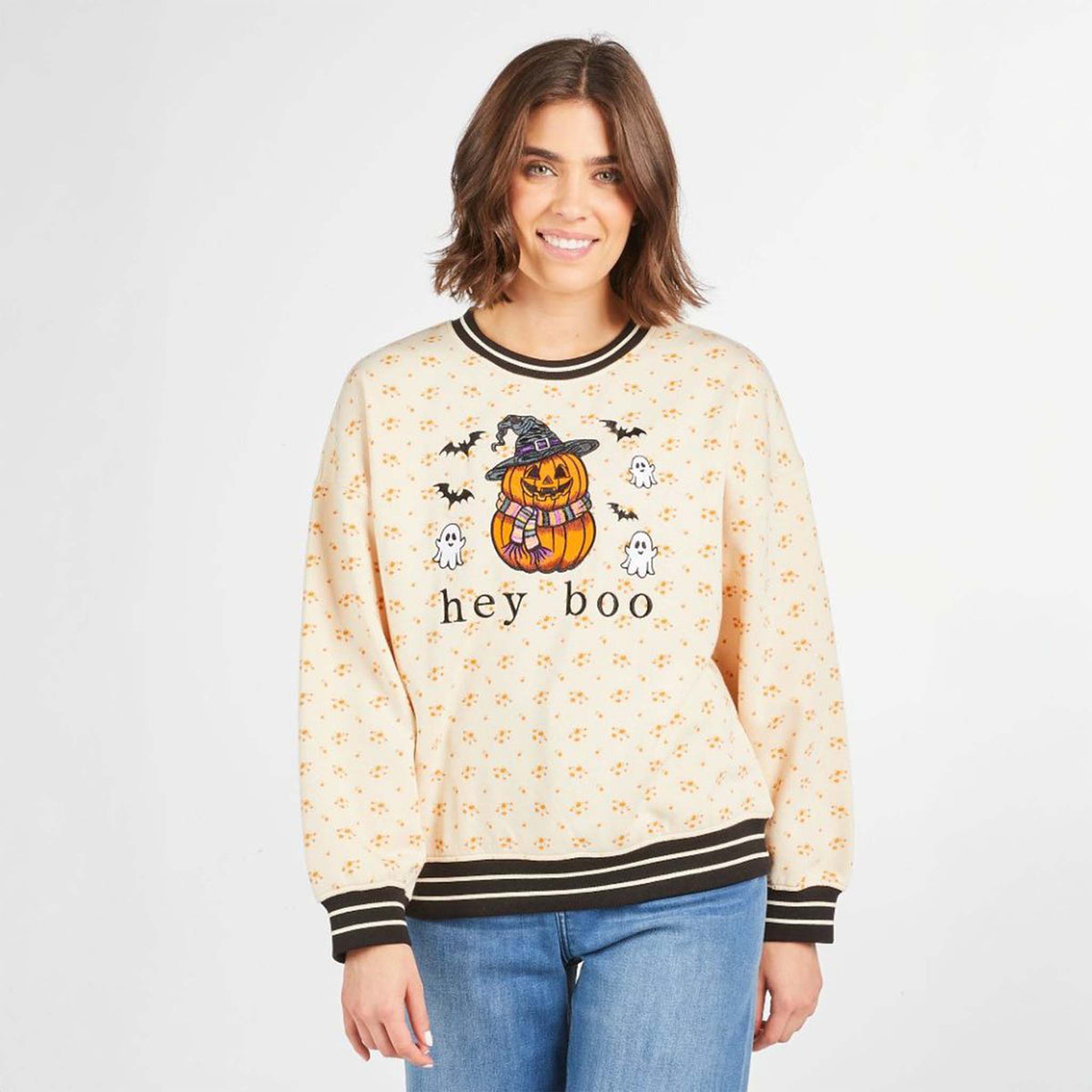 Model wearing beige floral 'hey boo' Halloween sweatshirt with pumpkin, ghosts, and bats graphic and striped varsity trim.