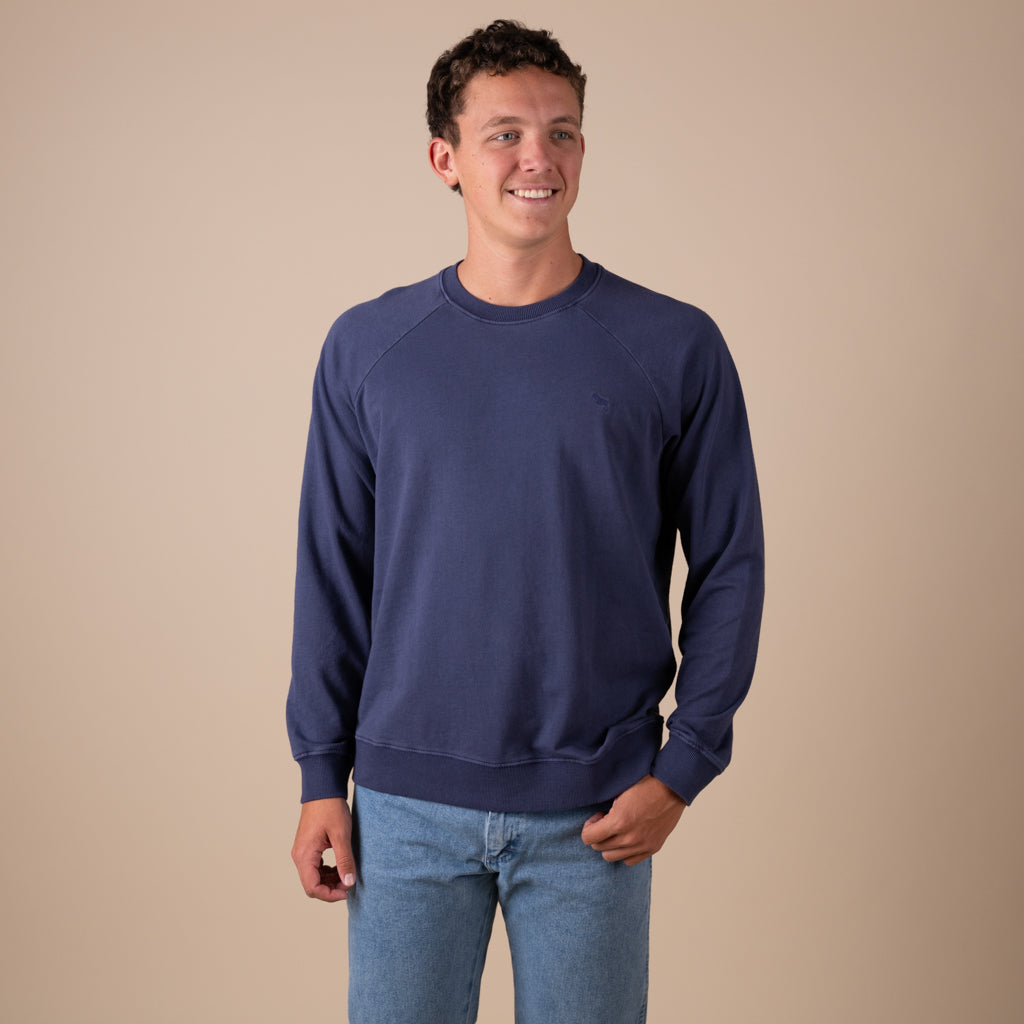 Man wearing a navy blue sweatshirt and jeans against a beige background