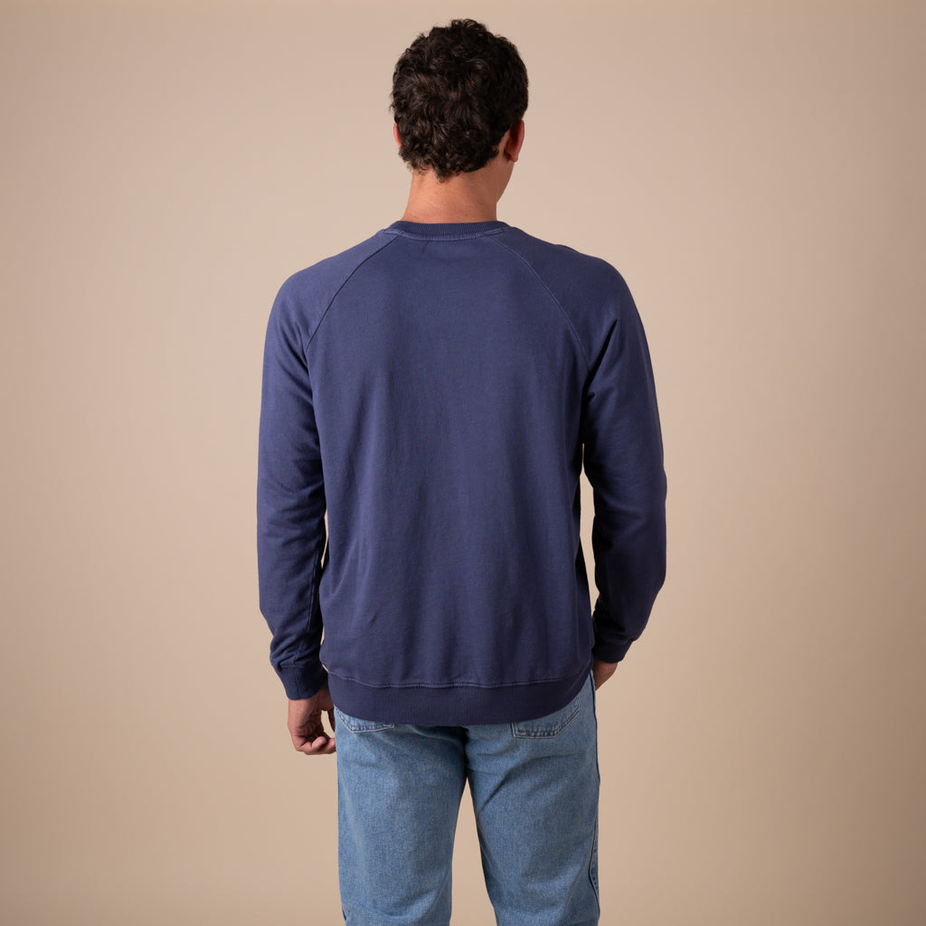 Man wearing a blue sweatshirt and jeans against a beige background