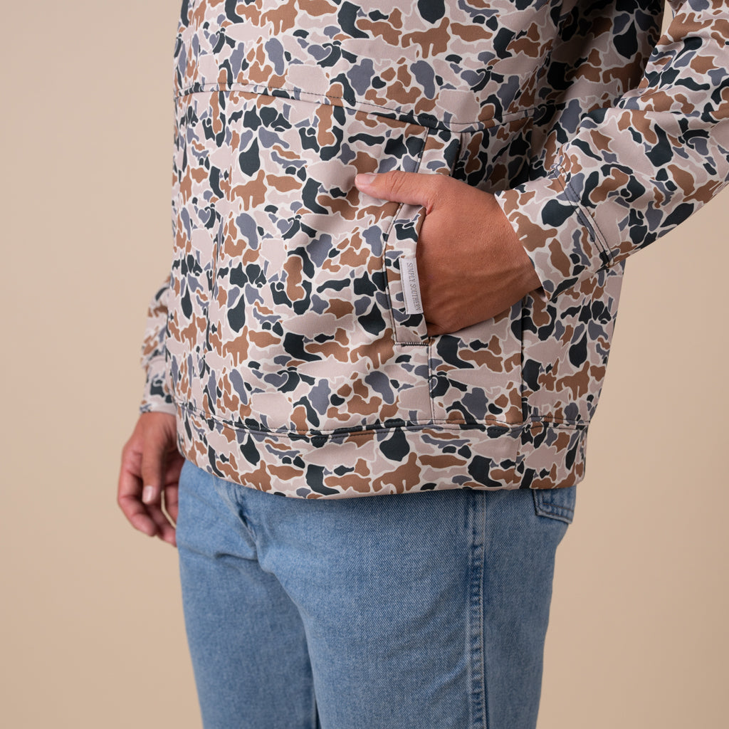 Person wearing a patterned shirt and blue jeans on a beige background