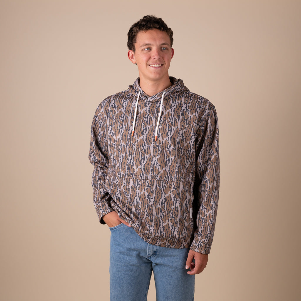 Man wearing a patterned hoodie and blue jeans against a beige background