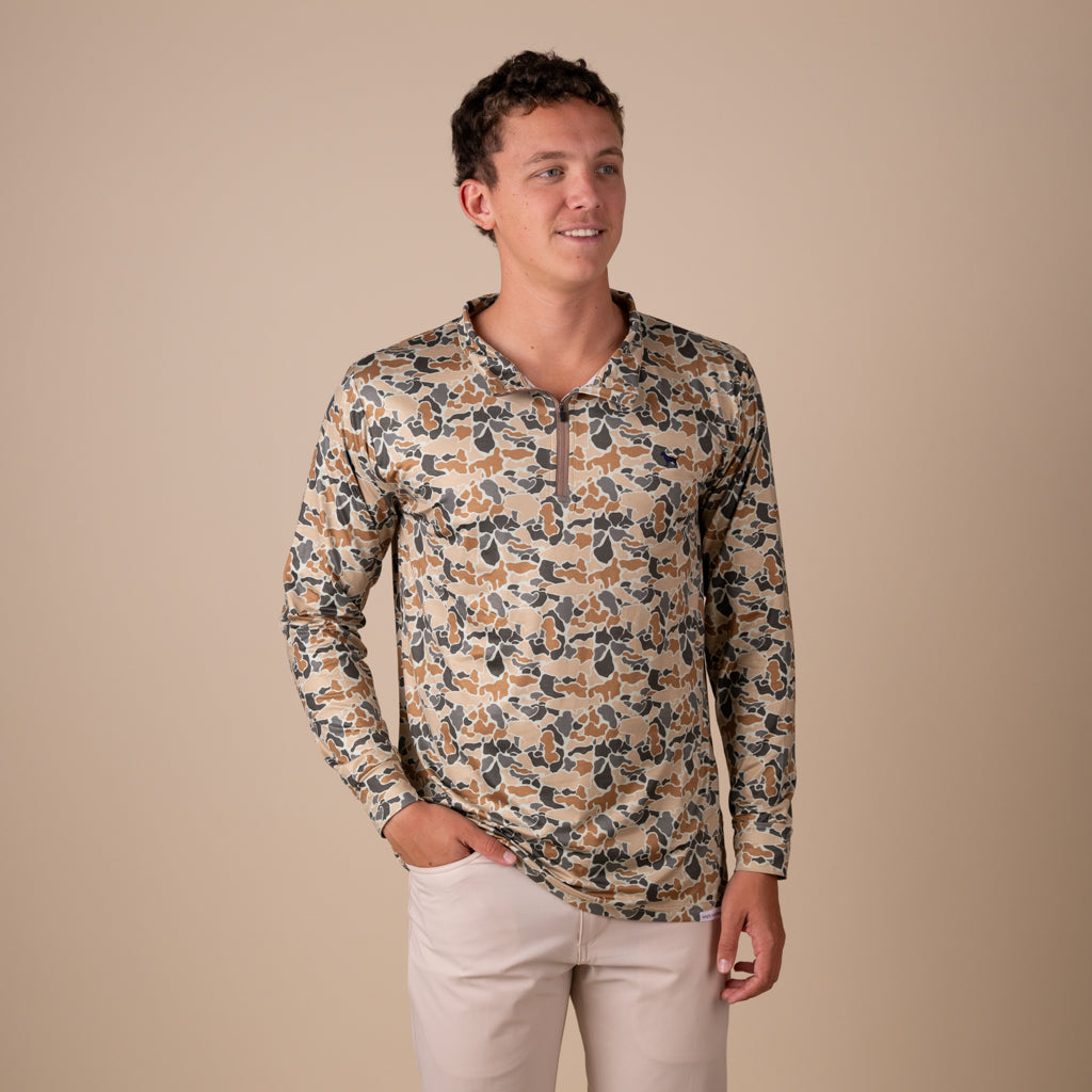 Man wearing a camo printed quarter zip pullover on a beige background.