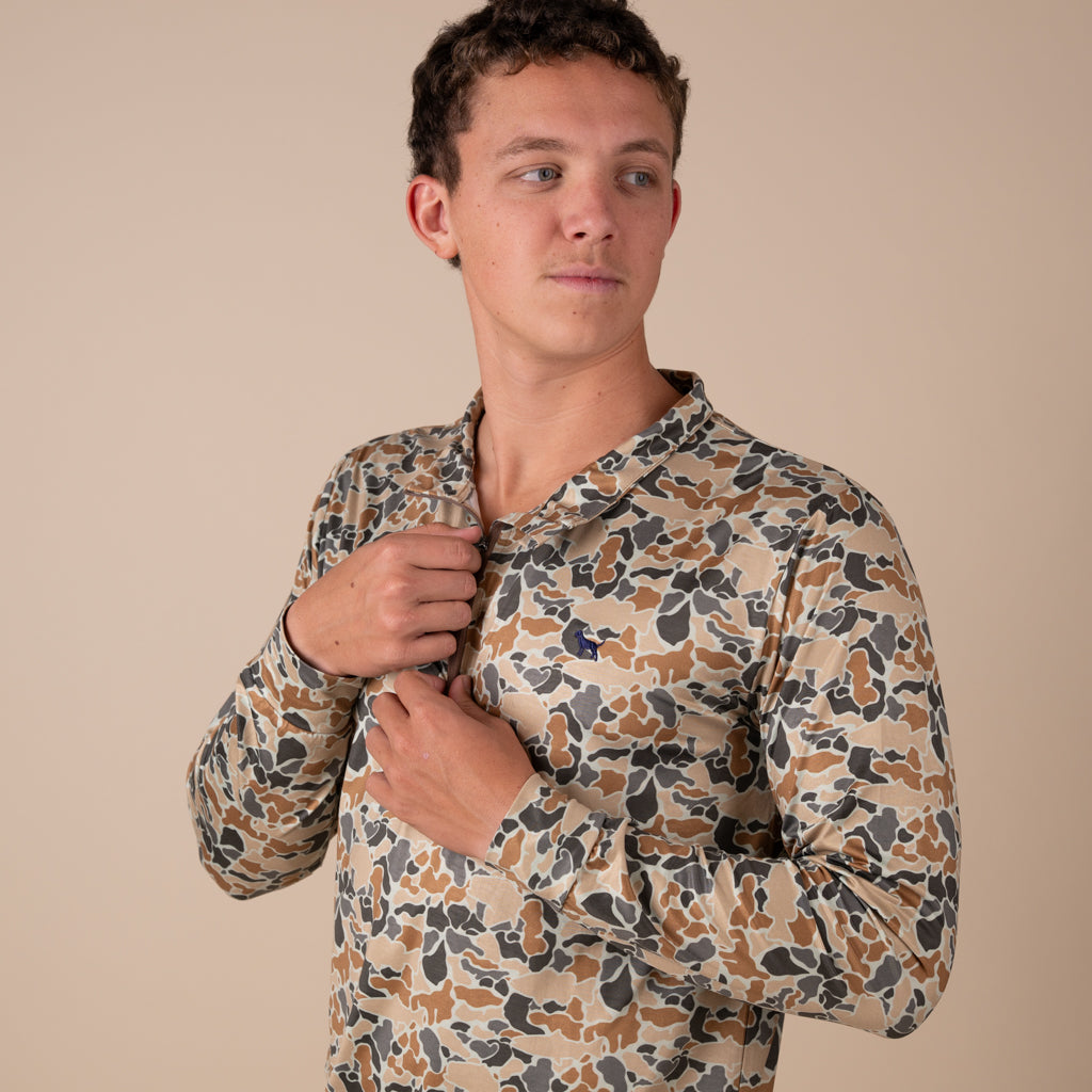 Man wearing a camo printed quarter zip pullover on a beige background.