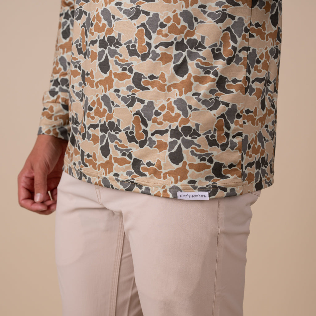 Man wearing a camo printed quarter zip pullover on a beige background.