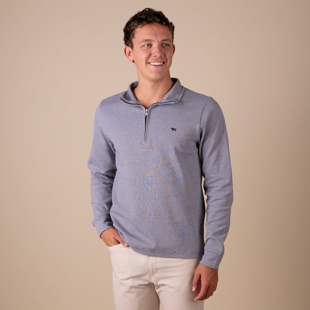 Man wearing a gray long-sleeve pullover with a small logo on a beige background