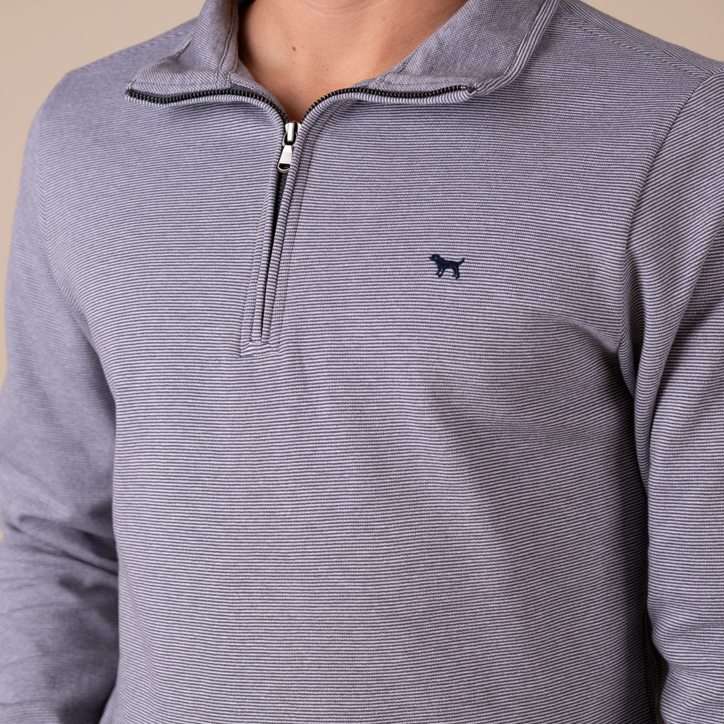 Close-up of a gray striped pullover with a small logo on a beige background