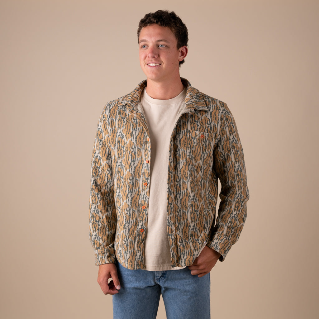 Man wearing a camo patterned shacket over a beige shirt on a beige background