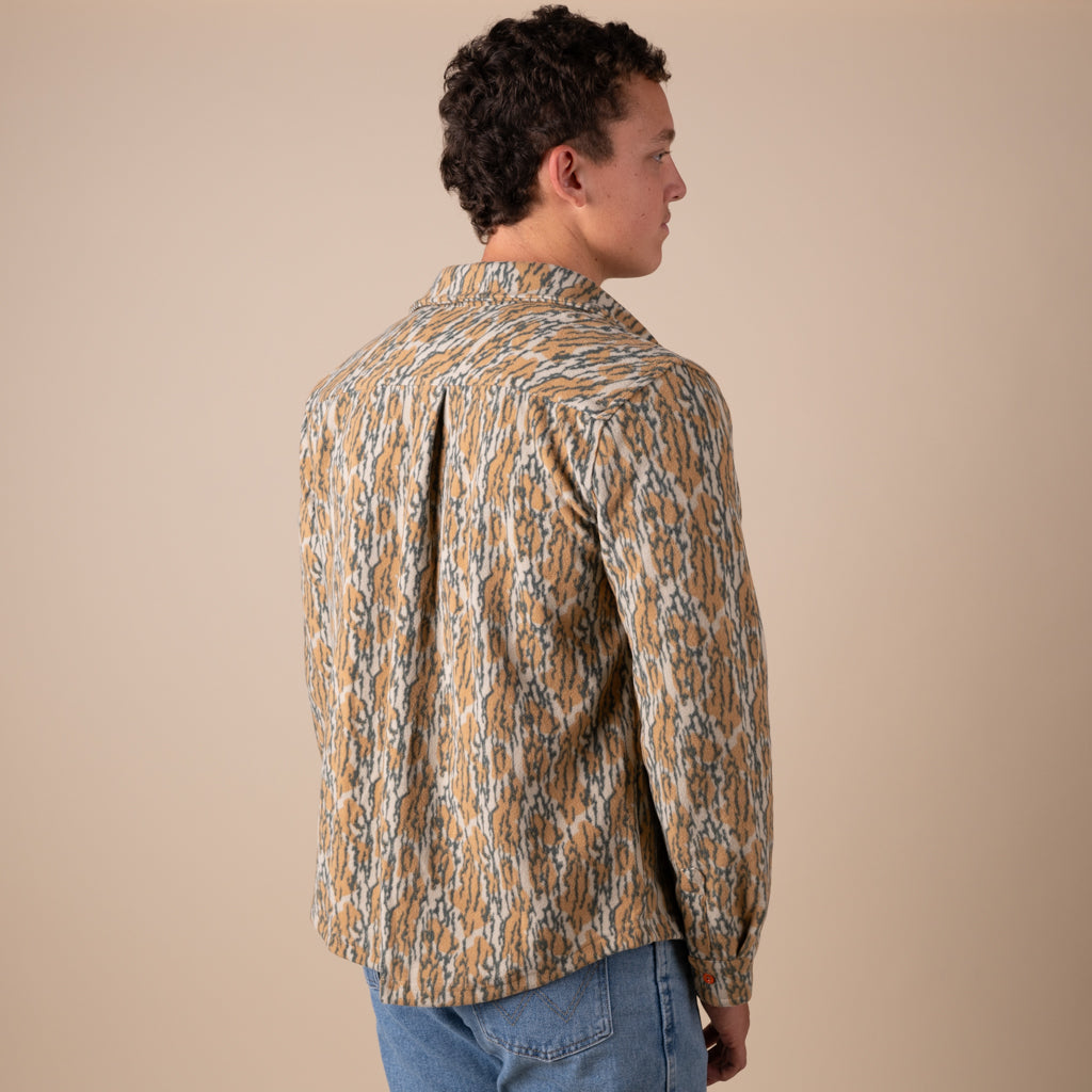 Man wearing a patterned shacket and jeans on a beige background