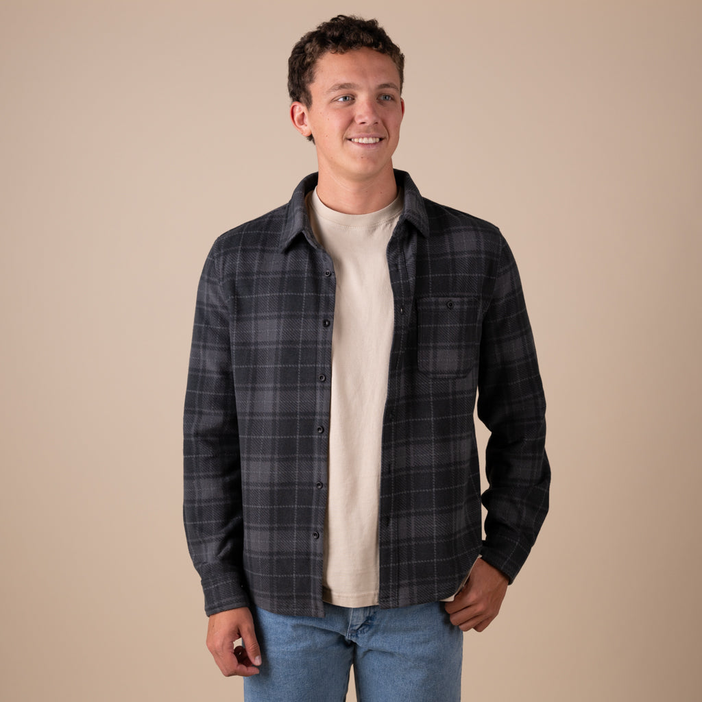 Man wearing a plaid shacket over a t-shirt with a beige background