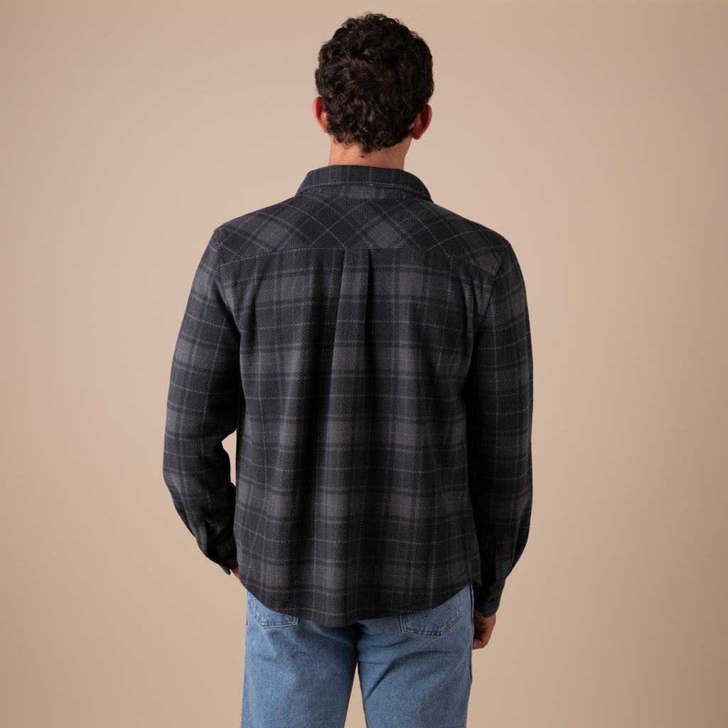 Man wearing a dark plaid shirt and blue jeans against a beige background