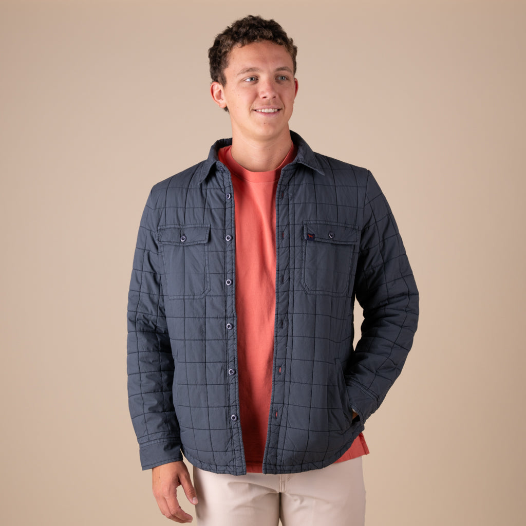 Man wearing a blue quilted shacket shirt over a red shirt on a beige background