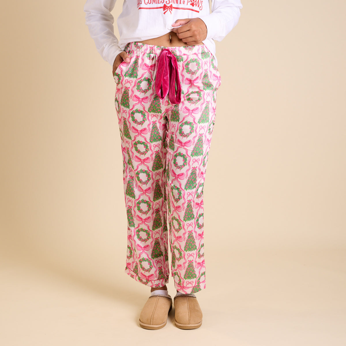 Front view of women’s Christmas pajama pants with festive tree and wreath pattern and pink velvet tie at waistband.