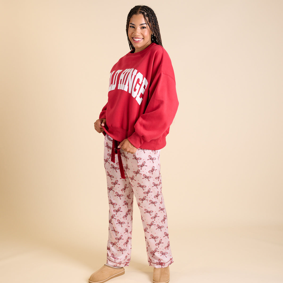 Woman wearing pink pajama pants with candy cane bow print and red drawstring tie.