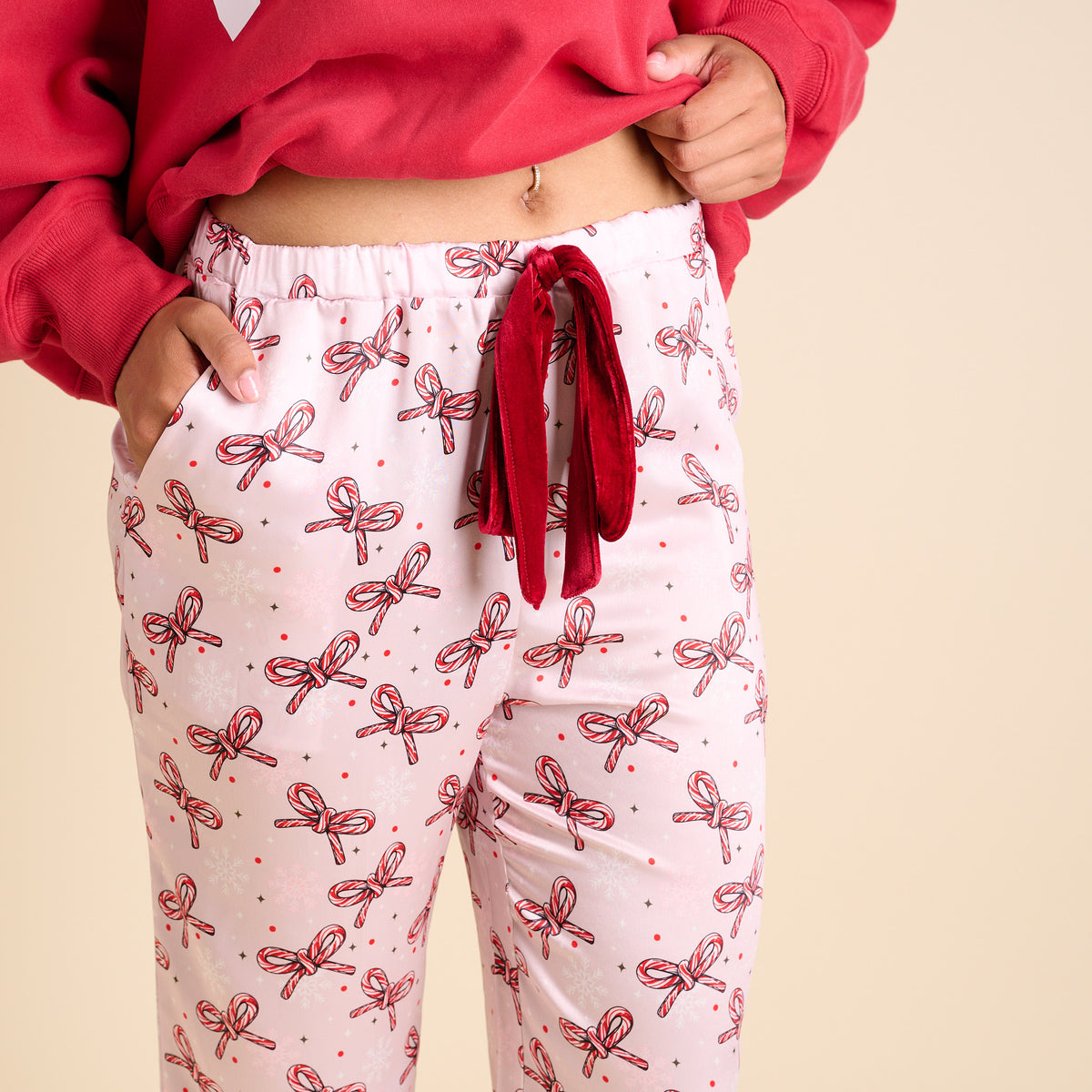 Close-up of pink pajama pants featuring candy cane bow print and velvet drawstring waistband.