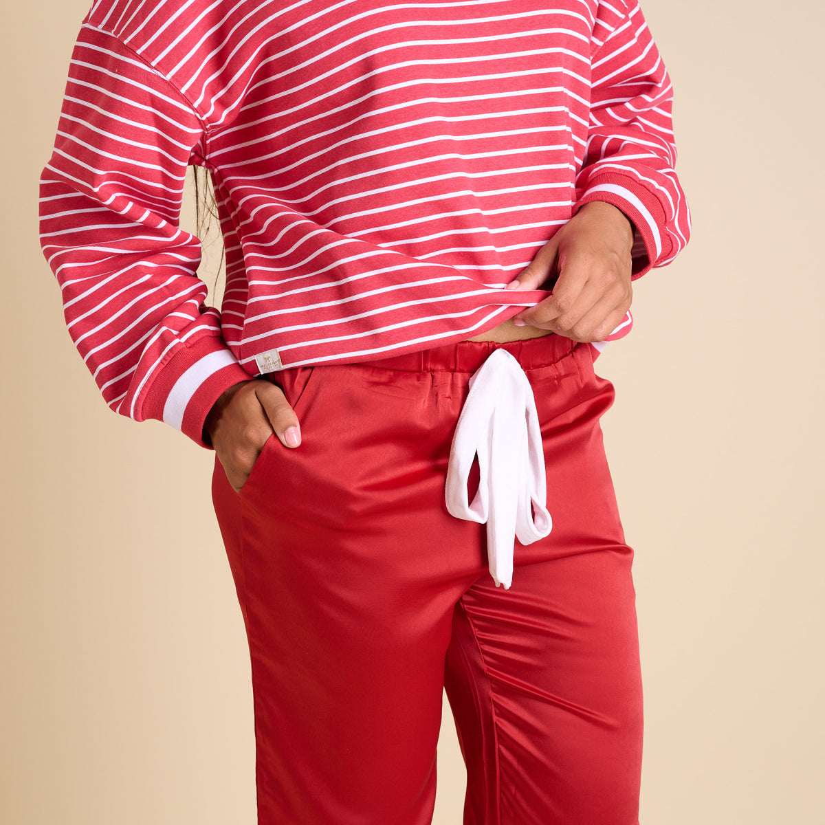 Red satin pajama pants with white drawstring waistband, styled with striped holiday top.
