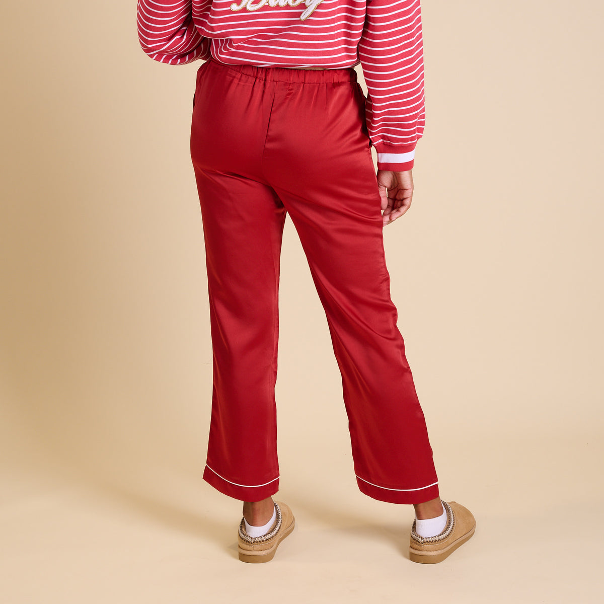 Back view of red satin pajama pants with elastic waistband and piping detail at hem.