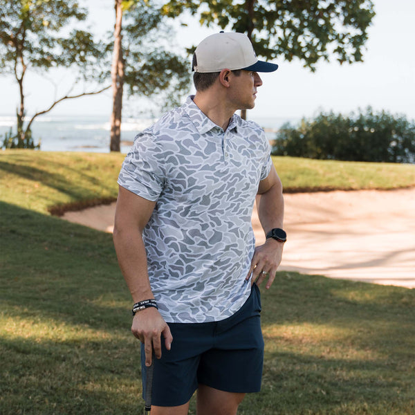 Man wearing Burlebo's White Camo Performance Polo standing on a golf course.