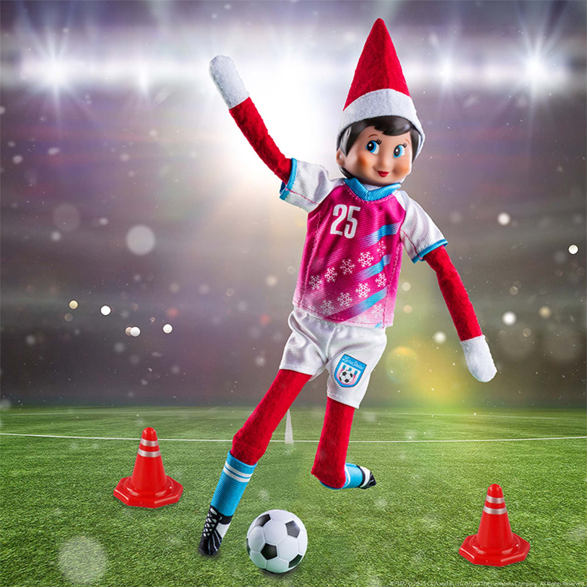 Elf on the Shelf in soccer gear on a football field with cones and a ball.