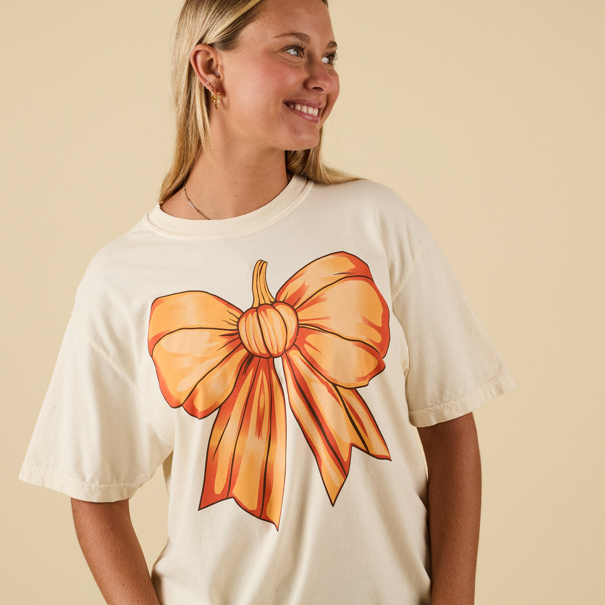 Close-up of ivory t-shirt with large orange pumpkin bow graphic on front.