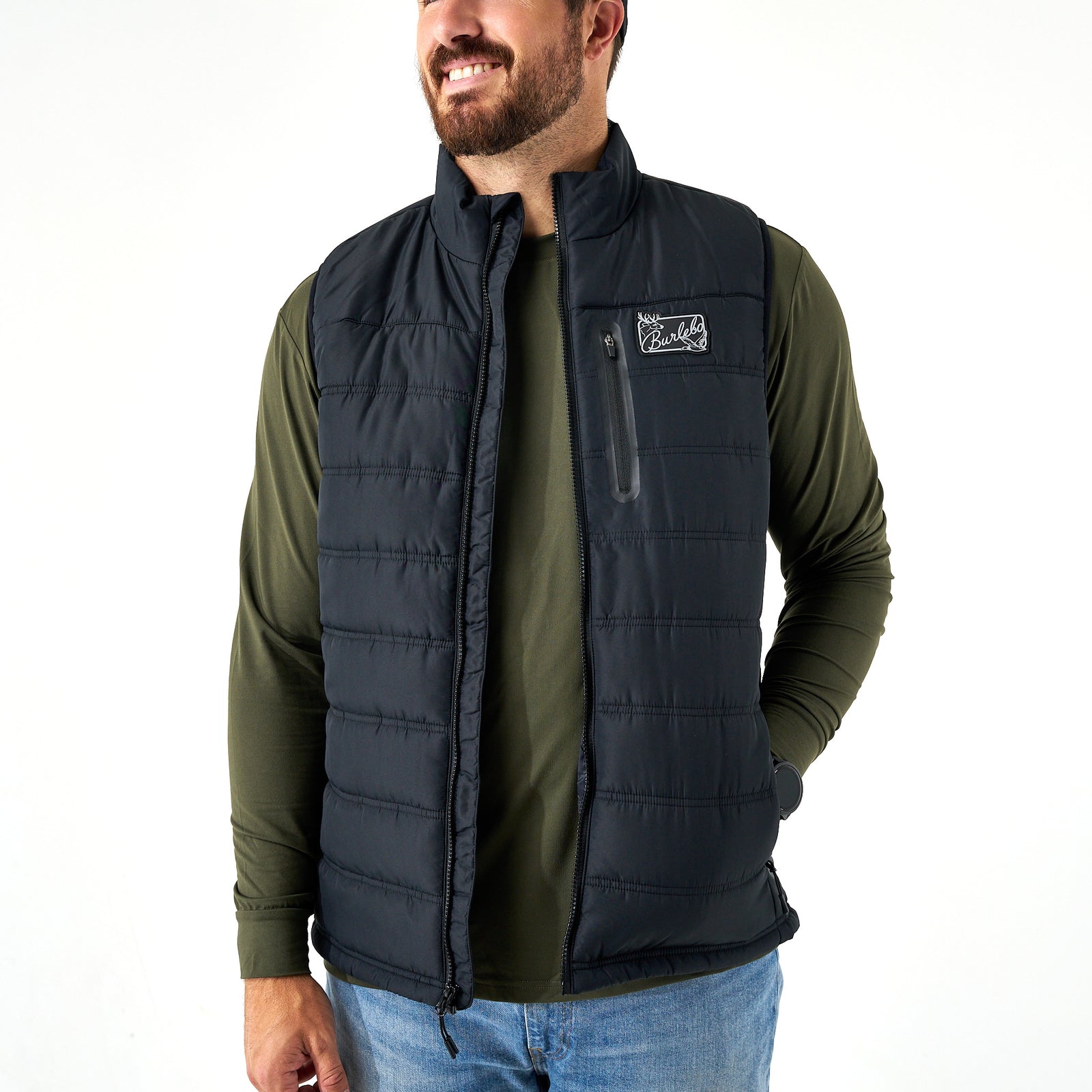 Man wearing a black puffer vest over an olive green long-sleeve shirt on a white background