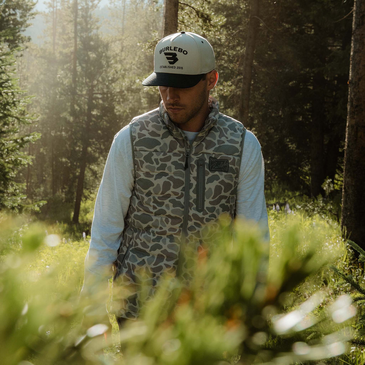 Man wearing a cap and patterned vest standing in a forest