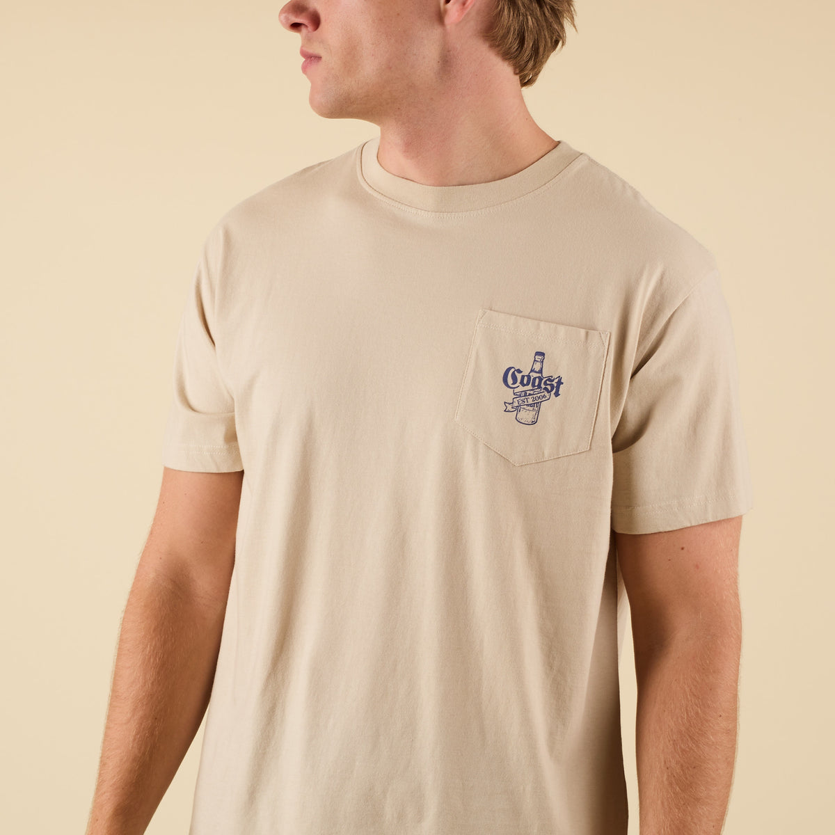 Front view of COAST Beer Barrel tee in sand with chest pocket featuring beer bottle logo graphic.