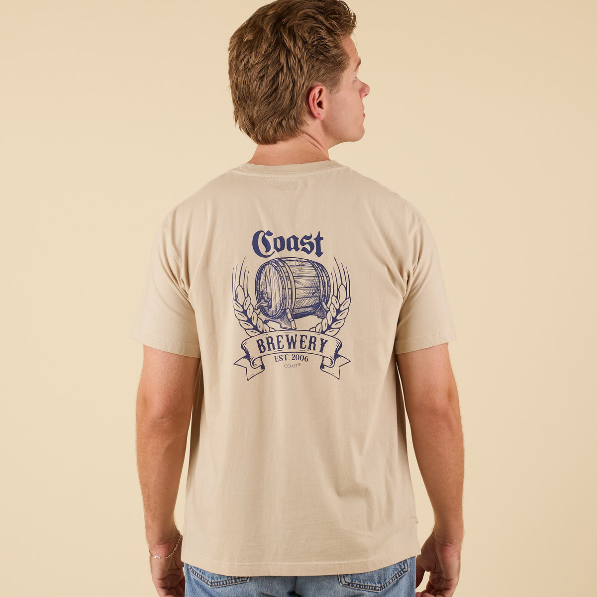 Back view of COAST Beer Barrel short sleeve pocket tee in sand with large brewery barrel graphic and wheat design.